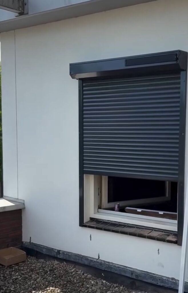 Antraciet rolluik, half open, op een witte gevel