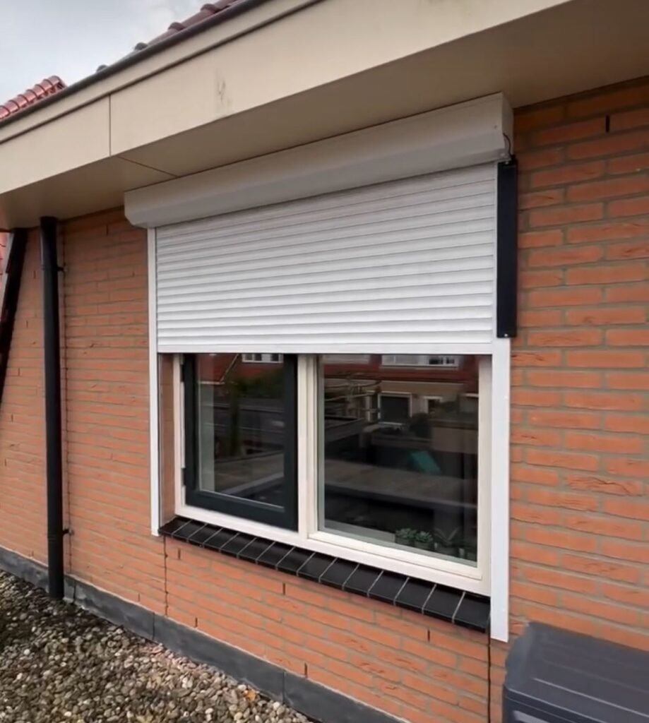 Wit rolluik, half open, op een rode bakstenen gevel