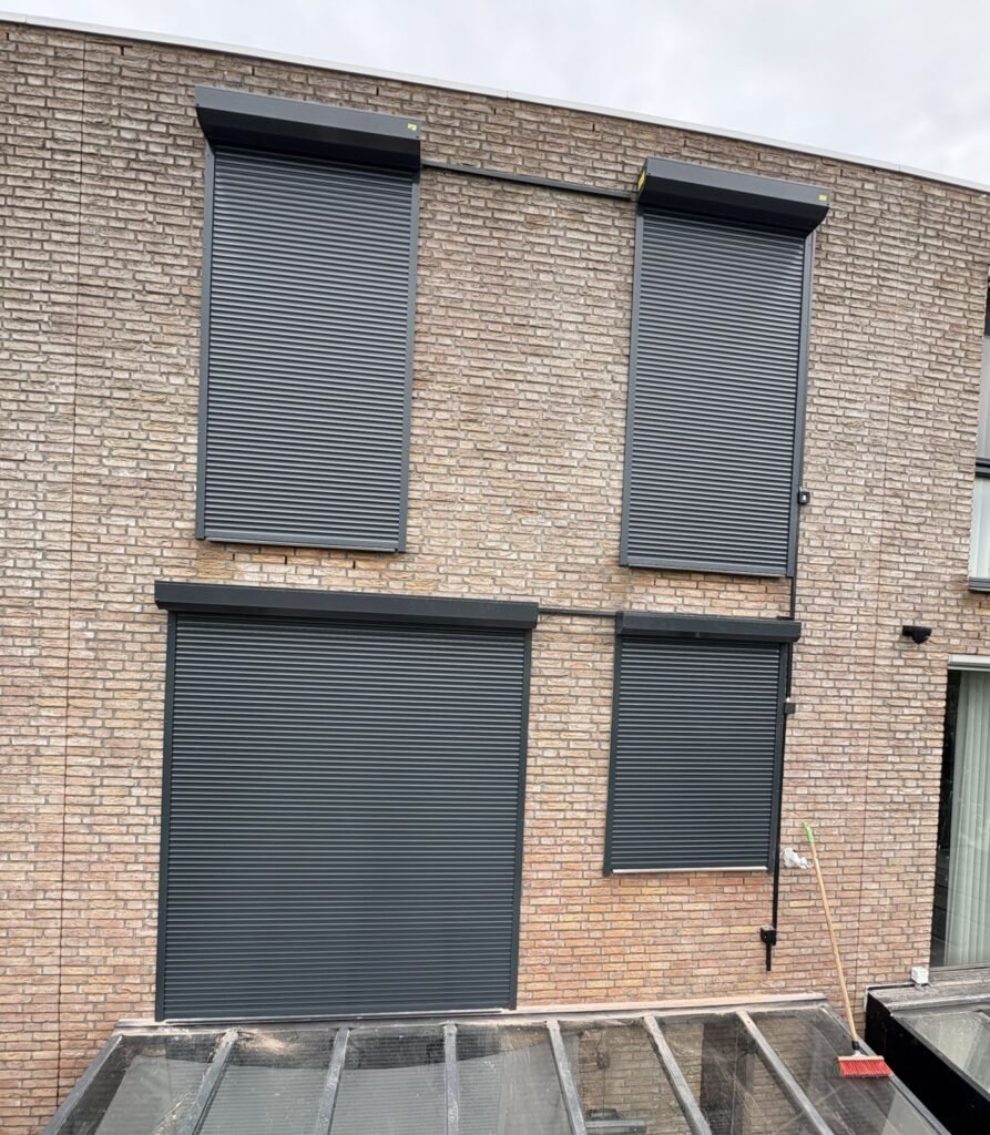 Vier antraciet rolluiken op een bakstenen achtergevel